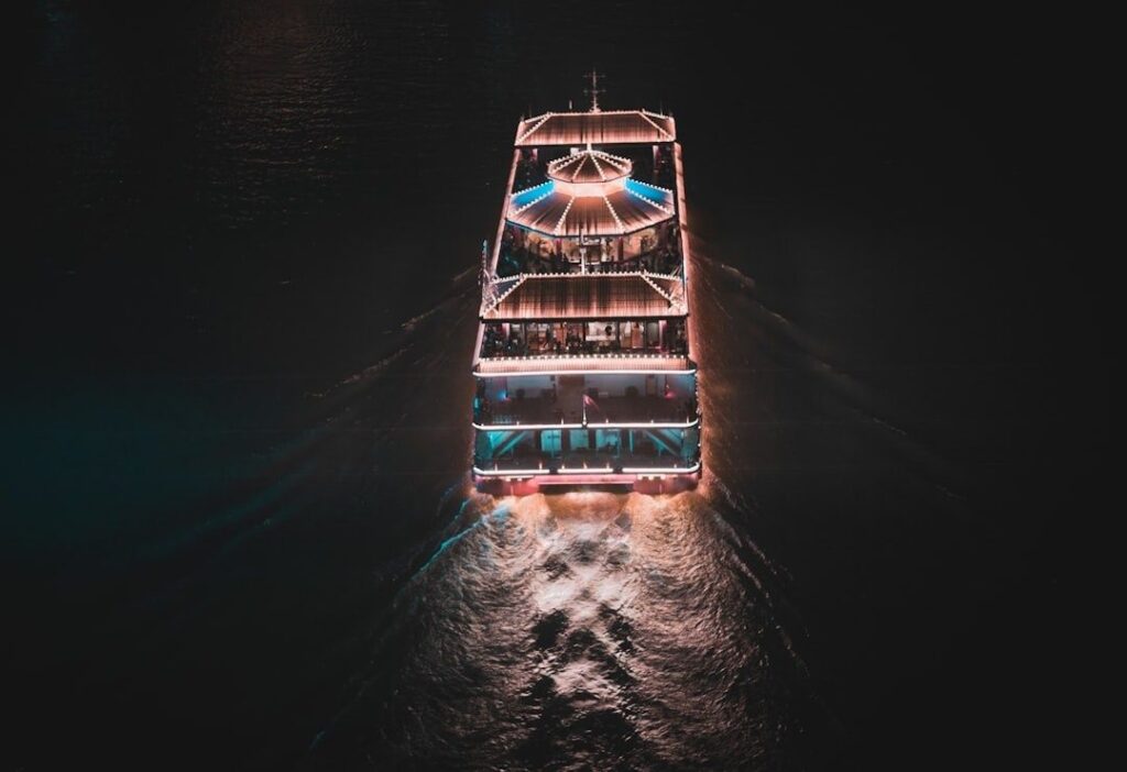 Verlicht passagiersschip vaart ’s nachts over donker binnenwater